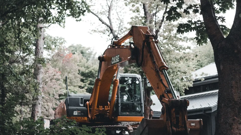 An excavator clearing brush and small trees from a wooded lot